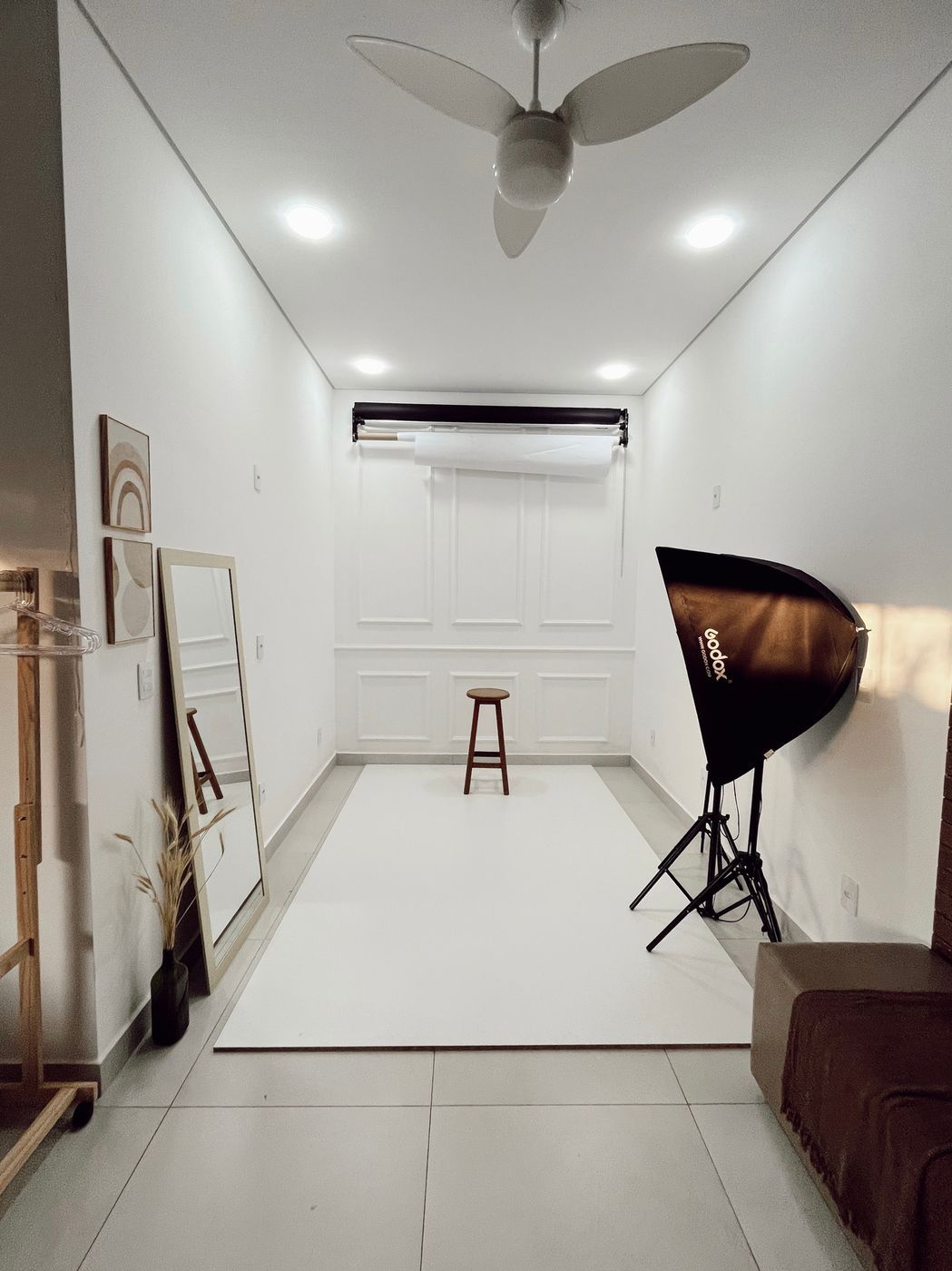 Sala do fundo infinito, com papel branco no chão, softbox, espelho de corpo inteiro e arara de roupas